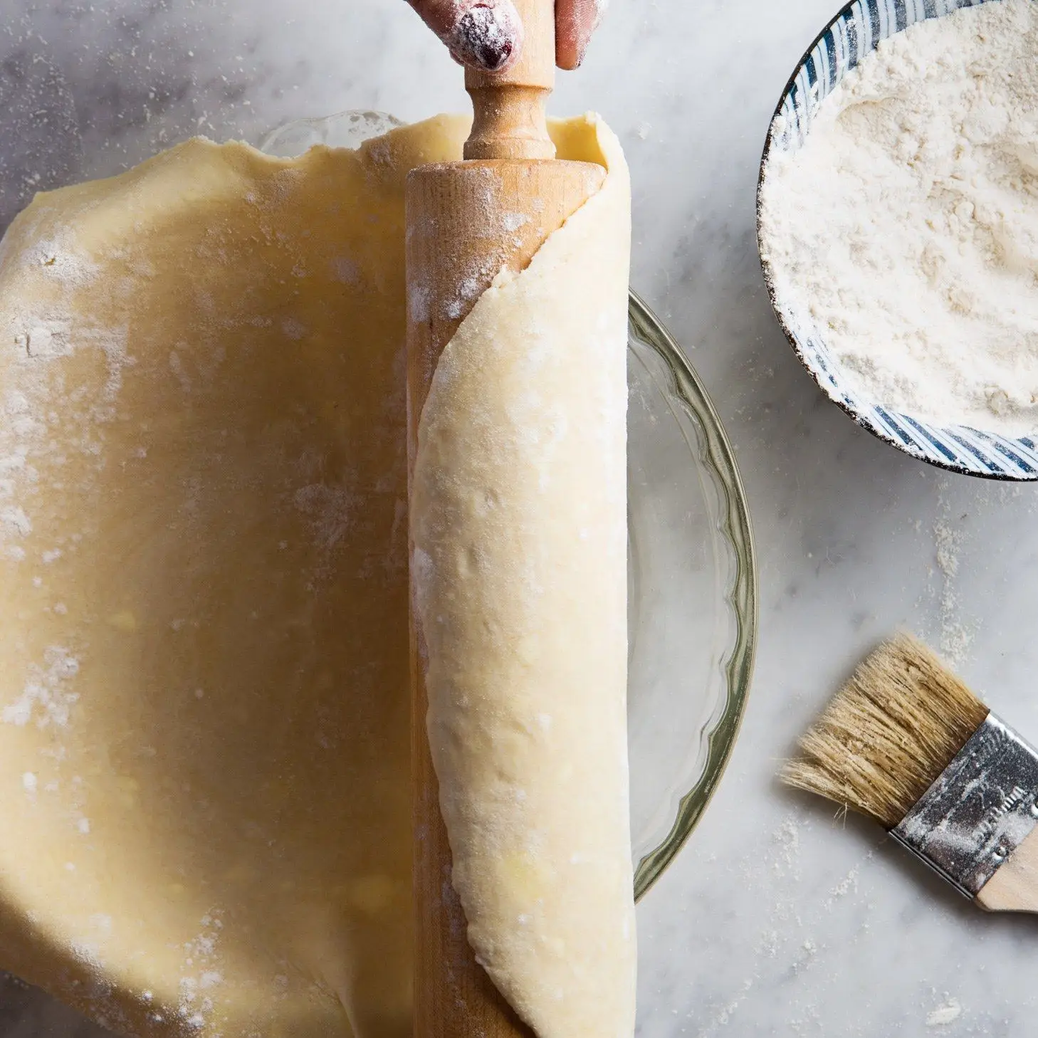 Pie dough rolled onto a rolling pin being transferred to a glass pie dish.
