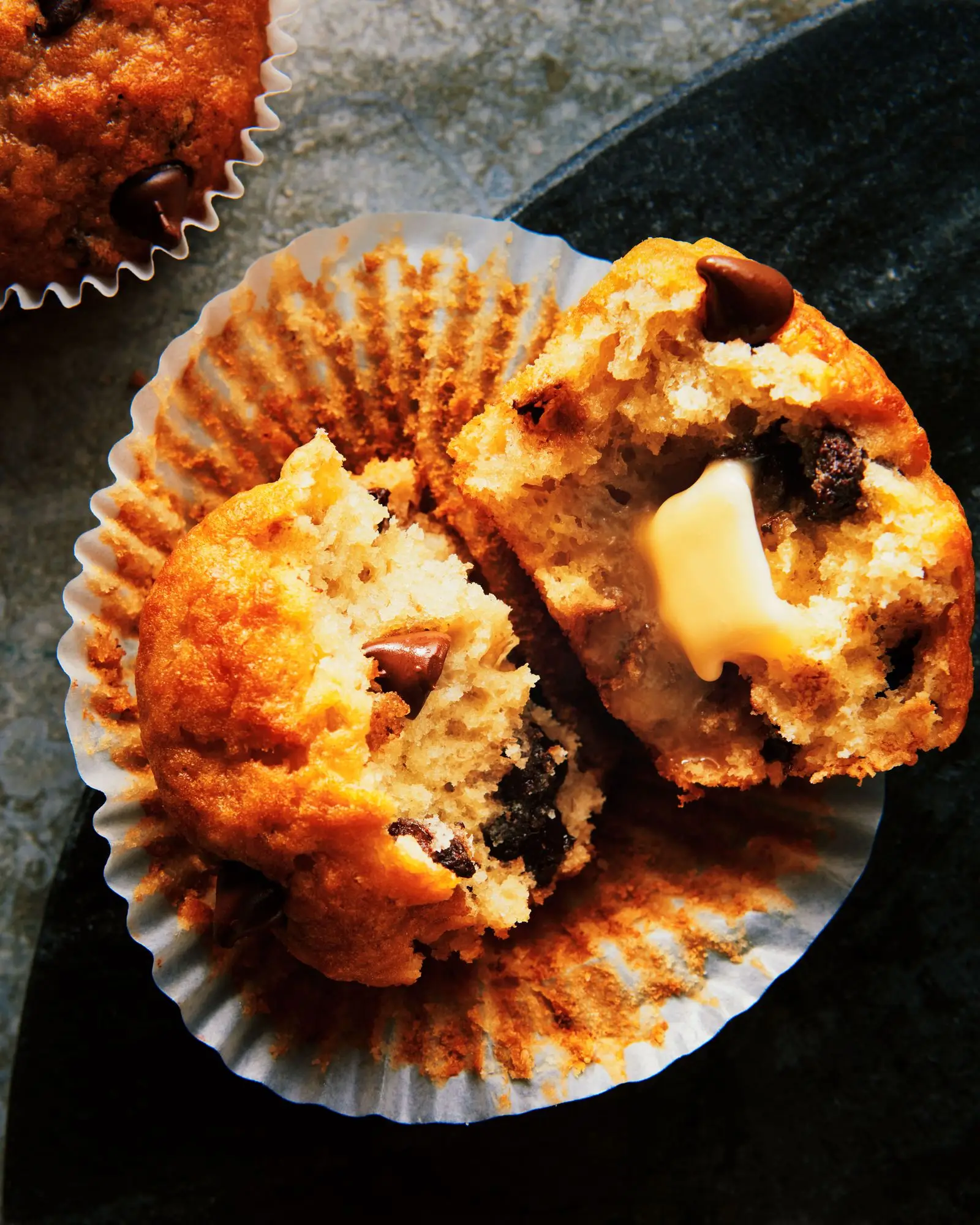 Banana chocolate chip muffins on a serving tray cut in half with melting butter.