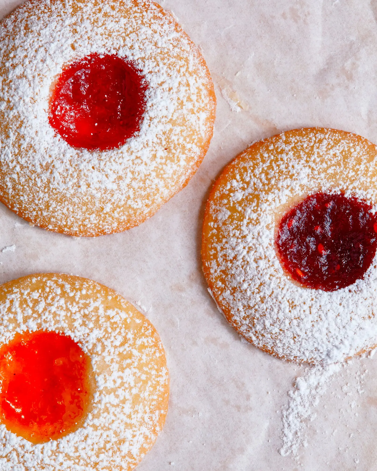 Three thumbprint cookies each filled with a different jam clockwise from the top left strawberry raspberry and apricot.