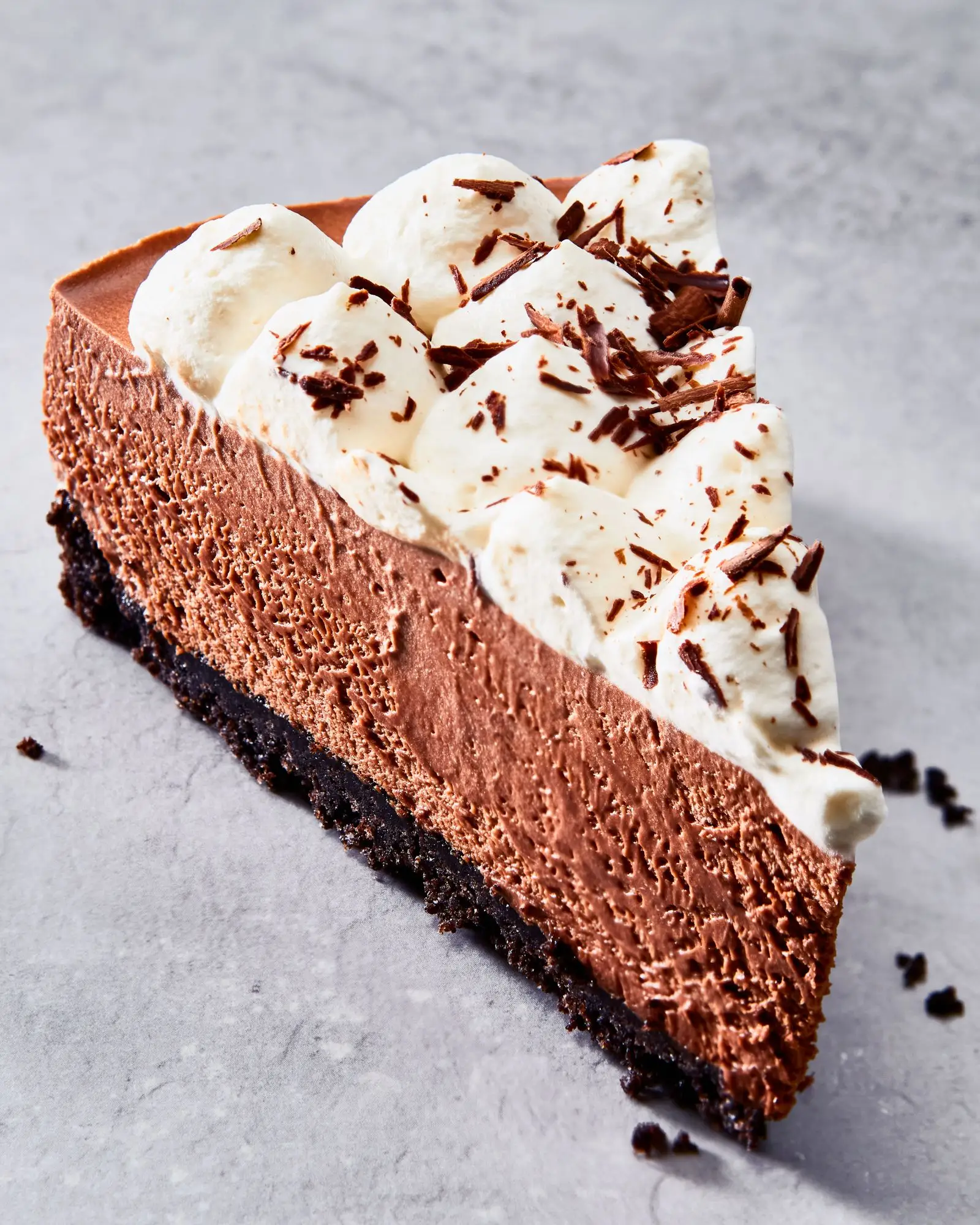 A slice of chocolate mousse pie with an oreo crust on a cake plate topped with whipped cream and chocolate shavings.