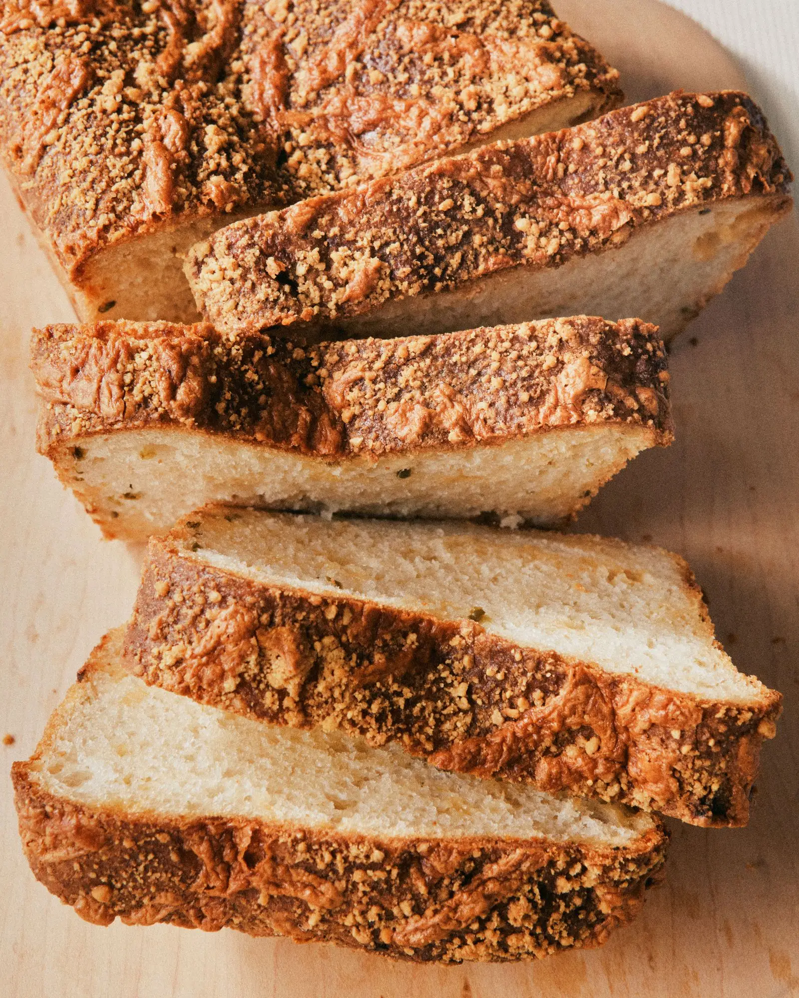 A sliced loaf of bread filled with cheddar cheese and diced jalapeño then topped with shredded ParmigianoReggiano.