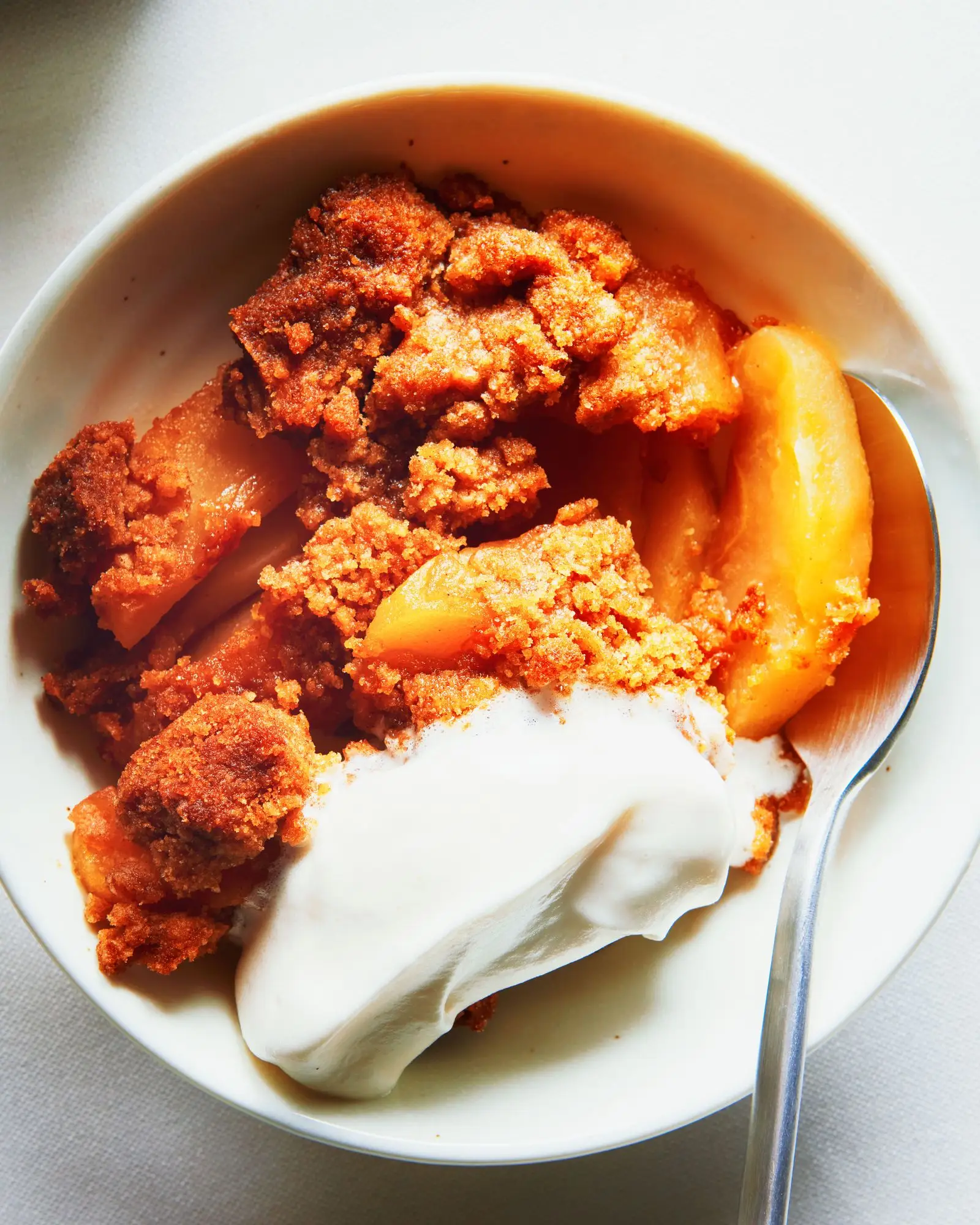 Baked flour butter and brown sugar over sliced apples in an bowl and topped with whipped cream.