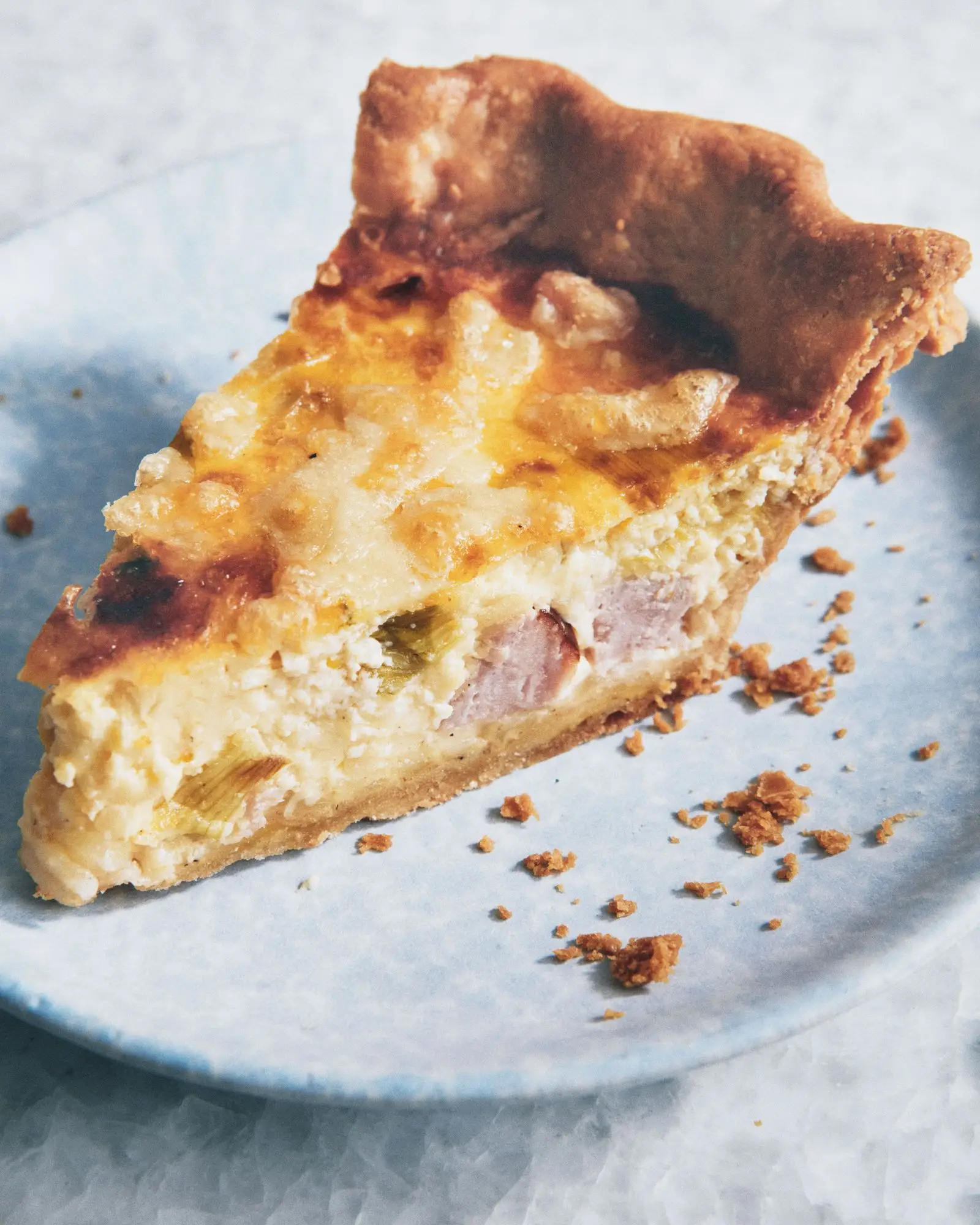 A slice of ham and cheese quiche with leeks on a plate.