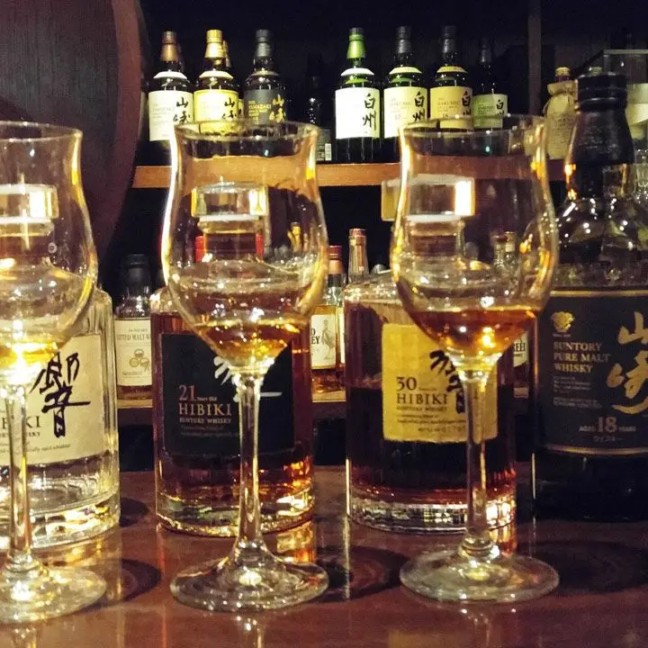 Hibiya Bar Whisky-S. Two tulip glasses are filled with a dram of whisky. Behind them are four bottles of Japanese whisky