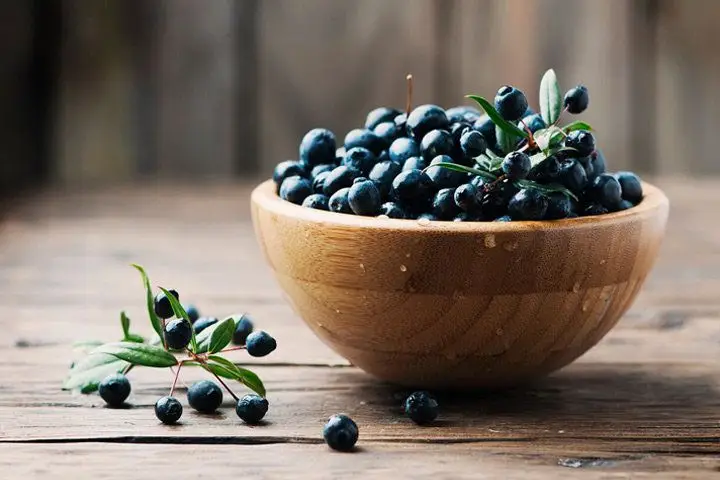 A wooden bowl of dark purple myrtle berries