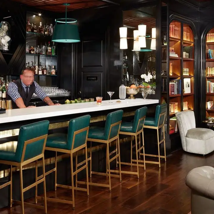 The Spectator Bar interior with teal-backed high stool at the bar and backlit bookshelves near the bar