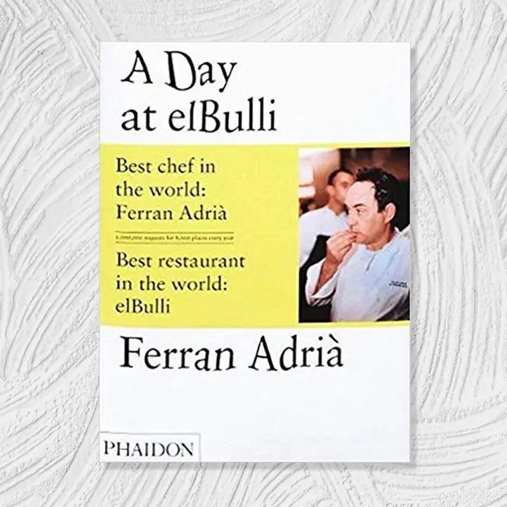 A Day at elBulli cover, white background with yellow color block and distorted black text alongside right-aligned photo of chef and author