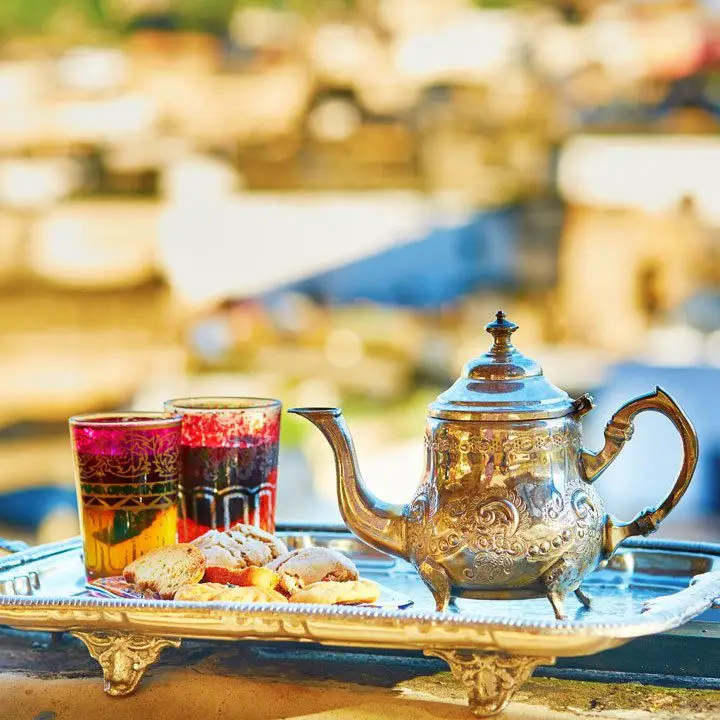 a silver ornate teapot on a silver serving tray, with red-tinted tumblers of mint tea