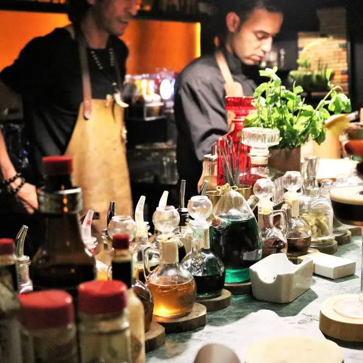 Baromètre Cocktail Lounge. Two bartenders, each in leather aprons, are preparing drinks behind a collection of tinctures and herbs