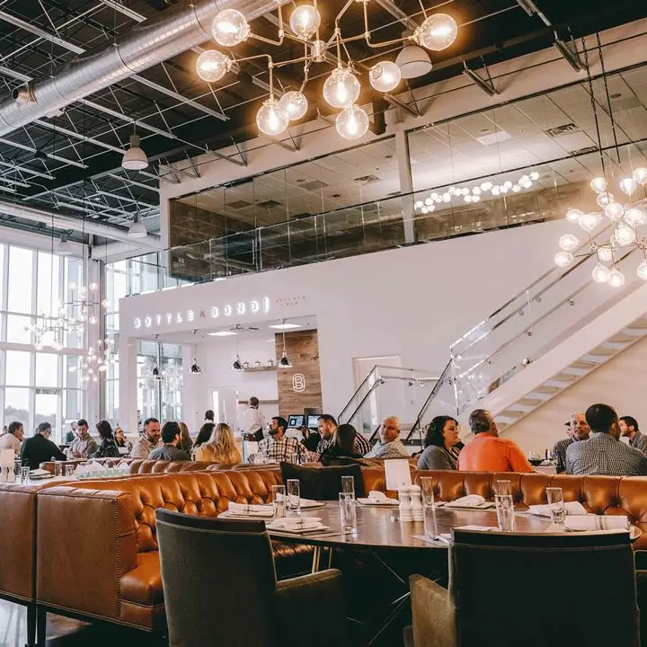 Kitchen & Bar at Bardstown Bourbon Company. Tufted gold banquettes anchor the ground floor and a staircase leads to a vantage point looking into the distlerry room with the stills