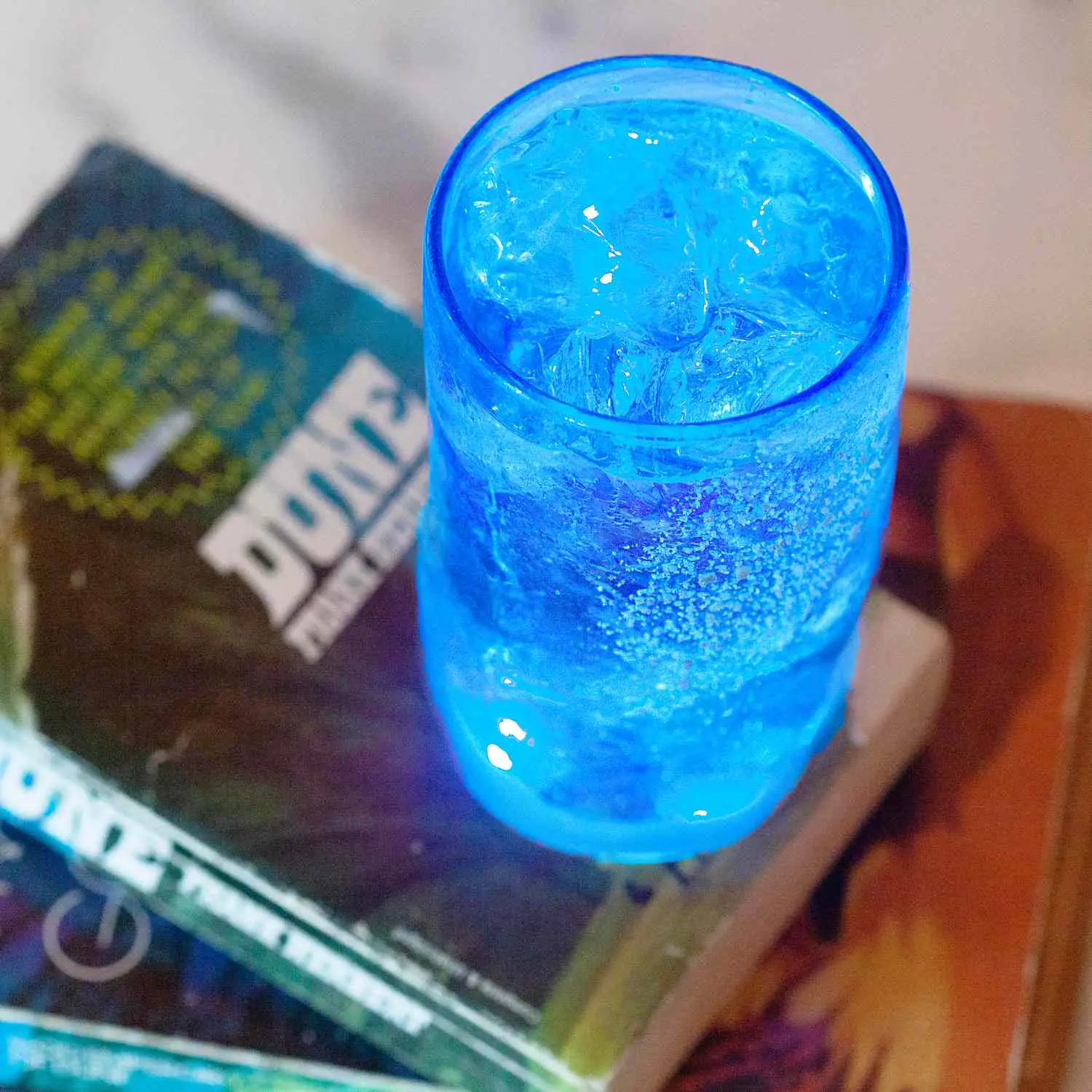 Highball cocktail glowing blue, sitting atop a copy of Frank Herbert