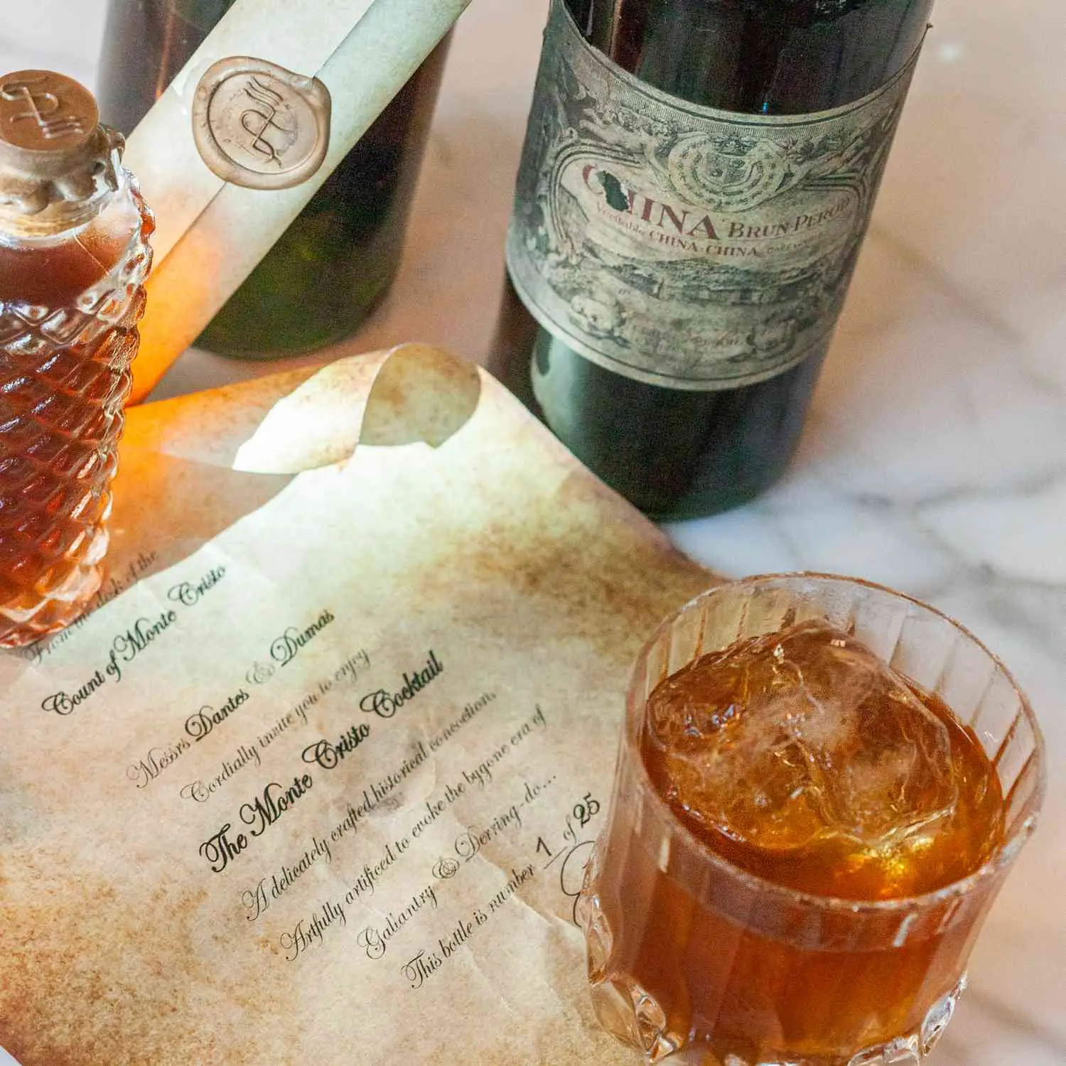 Wax-sealed bottle and rocks glass containing the Monte Cristo cocktail, sitting atop an imitation manuscript of The Count of Monte Cristo