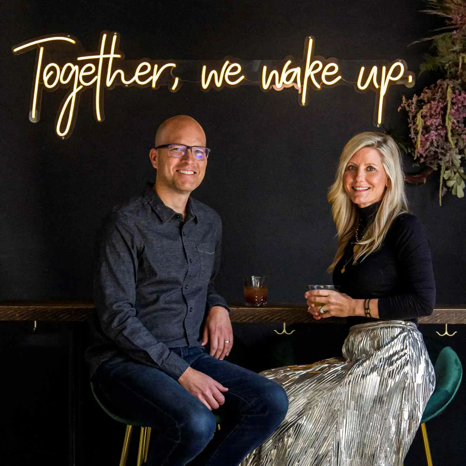 Owners Billy and Christy Wynne, of Awake in Denver, Colorado, seated, in front of neon sign that says 