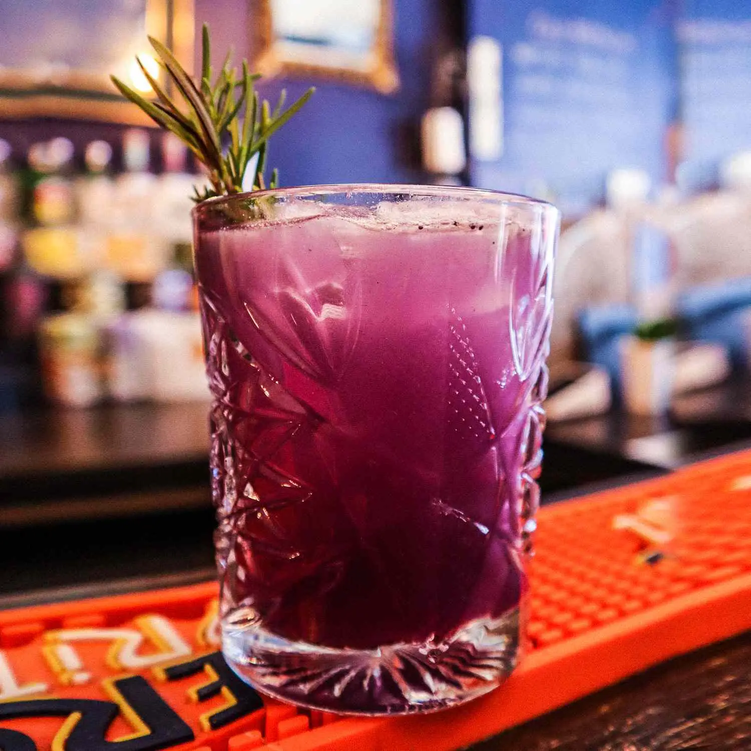 Vibrant purple drink, called The Healer, with rosemary sprig on bar top at Hekate