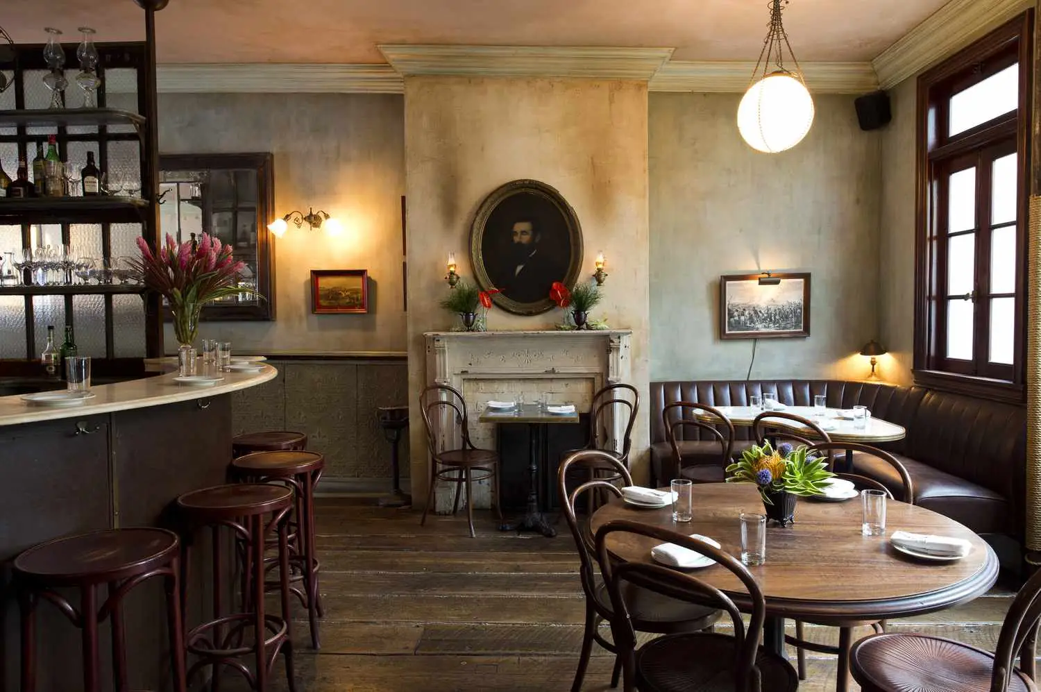 Maison Premiere interior, showing wood tables, chairs, and ornamental fireplace