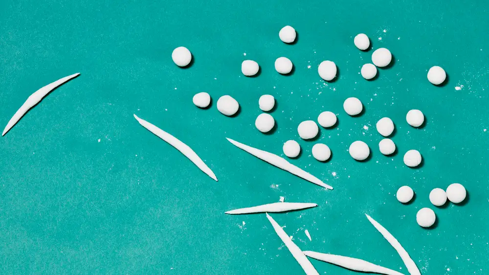 Two hands rolling balls of dough into noodles