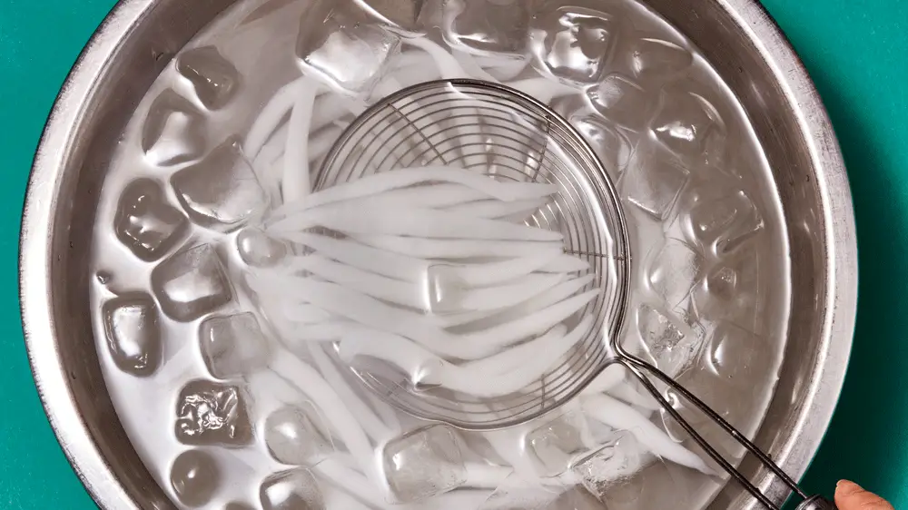 A spider strainer lifting noodles out of an ice bath.