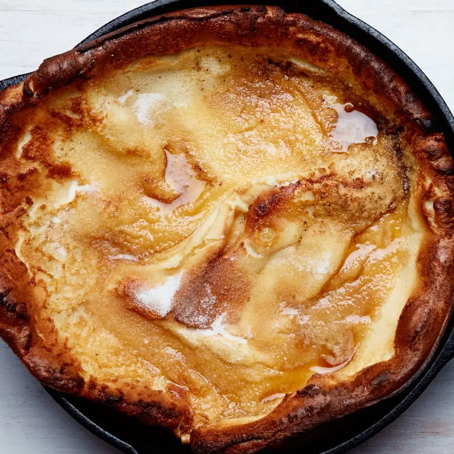 Overhead view of a crinkly Dutch baby in a cast iron skillet with pools of browned butter.