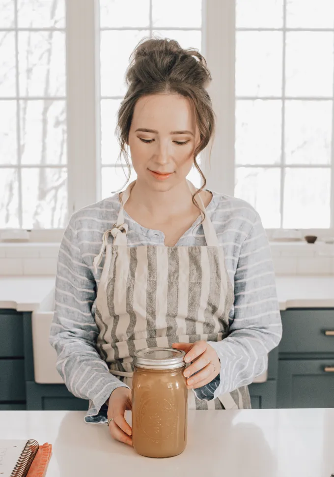 Woman holding a jar of homemade chicken feet bone broth.' title='Chicken Feet Bone Broth Recipe