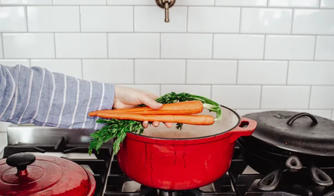 Adding carrots to a red Dutch oven.' title='Chicken Feet Bone Broth Recipe