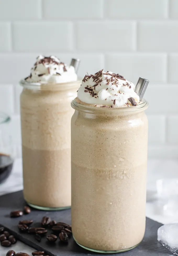 Two cups of mocha frappuccino on a slate board with coffee and ice cubes around it.' title='Mocha Frappuccino Recipe