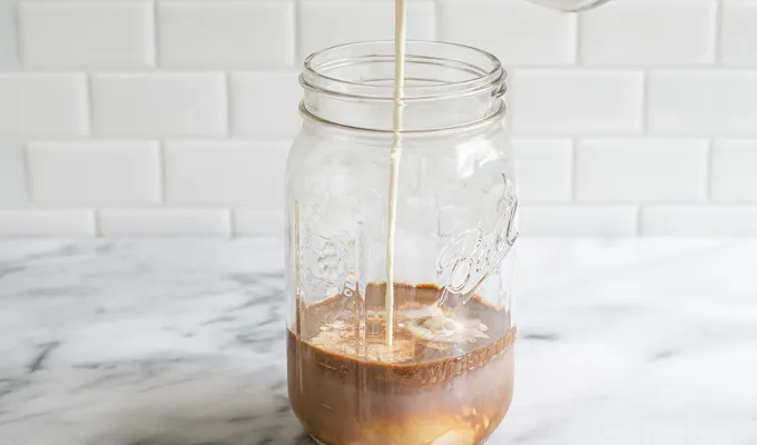 Pouring cream over the chocolate milk coffee and vanilla in a mason jar.' title='Mocha Frappuccino Recipe