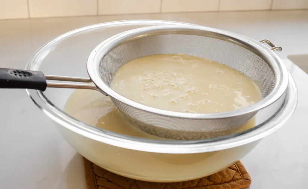 Straining the cooked eggnog custard to remove any lumps.' title='Homemade Eggnog