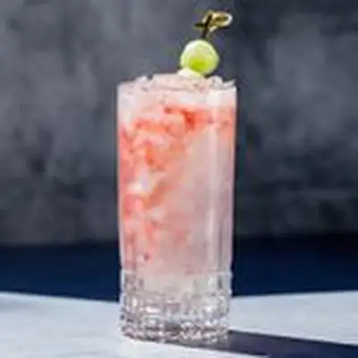 A Collins glass containing a translucent white cocktail with swirls of red raspberry liqueur, garnished with a skewered honeydew melon ball
