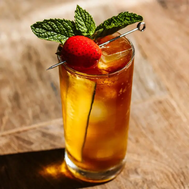 Pimms Cup in highball glass garnished with strawberry mint and cucumber spear