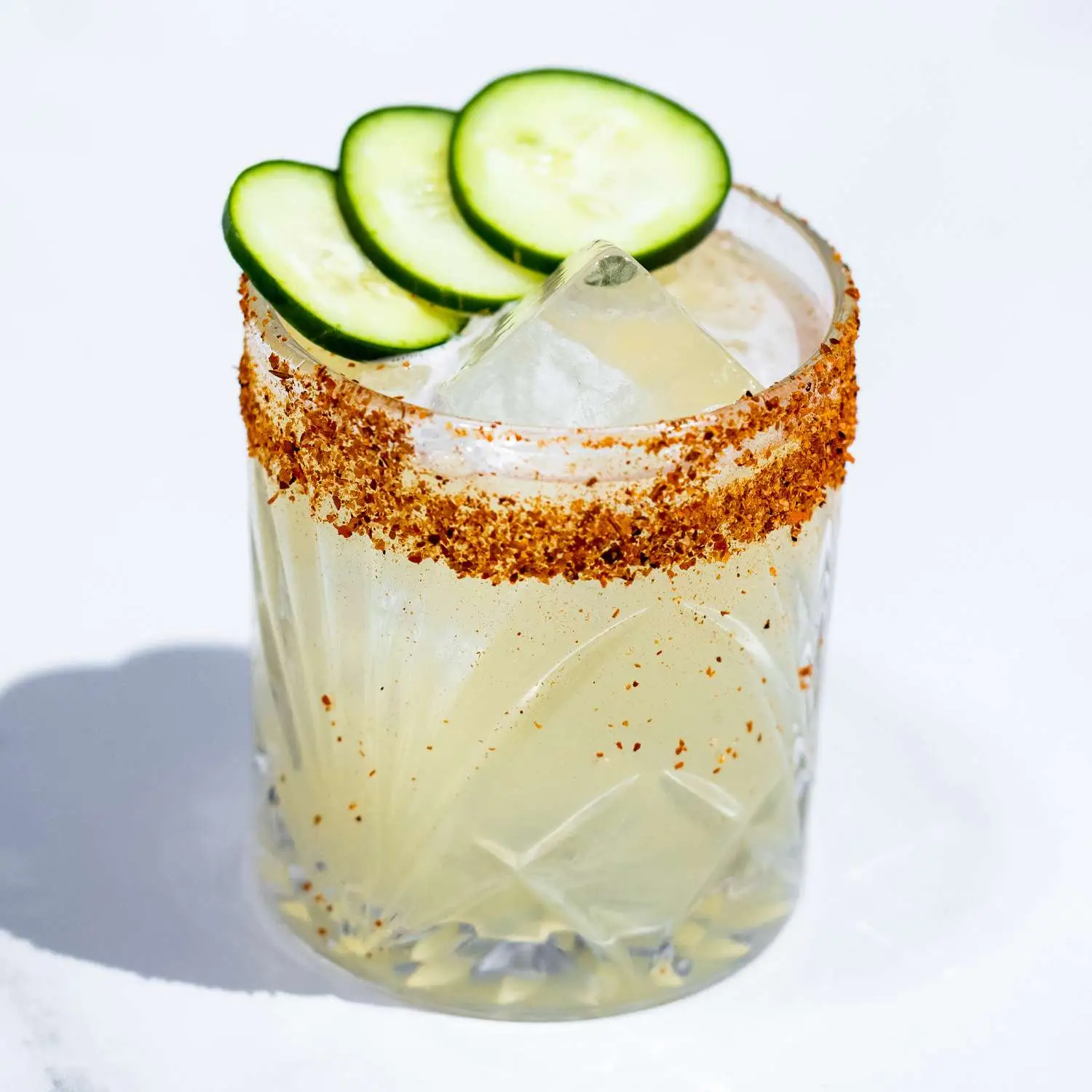 El Pepino cucumber margarita cocktail in rocks glass with a spicy salt rim, garnished with three cucumber slices, on white marble background