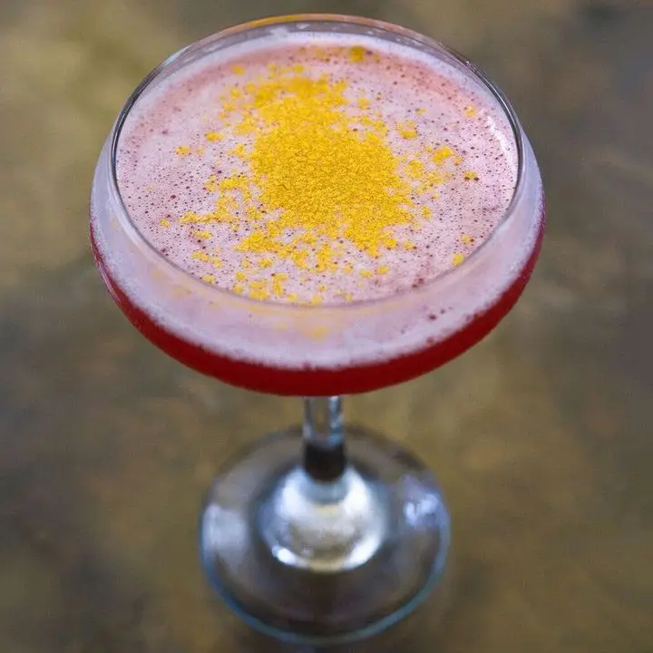 A top down shot of a cocktail coupe filled with a red drink topped with gold flakes. 