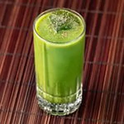 green-colored John the Baptist cocktail in a Collins glass, served over ice and dusted with fresh nutmeg