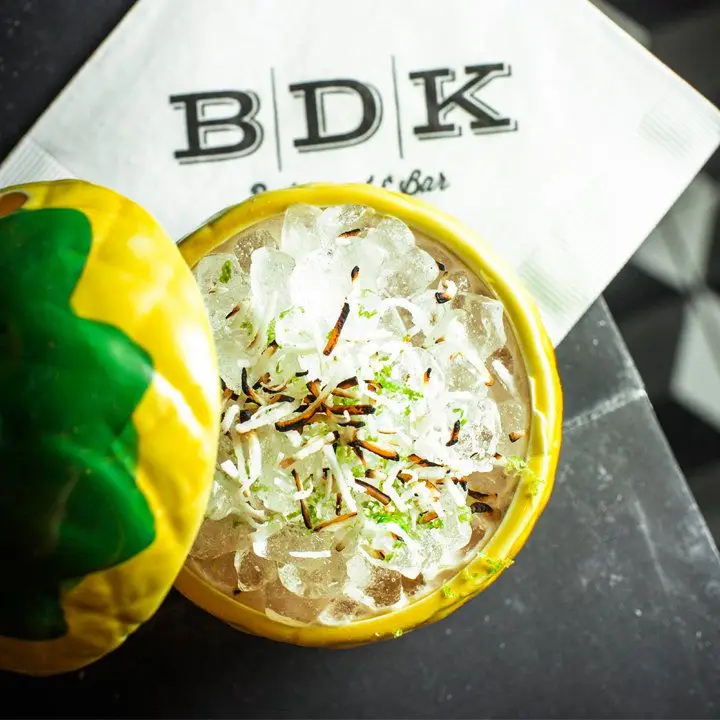 lychee cocktail in a yellow pineapple mug, garnished with toasted coconut and lime zest