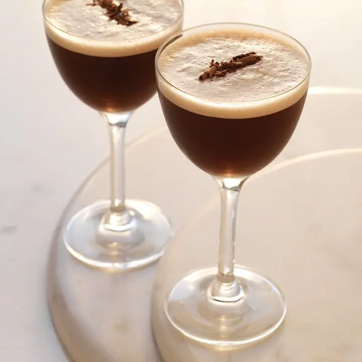 Two Chocolate Martinis in nick and nora glasses with foam and chocolate shavings on marble surface 