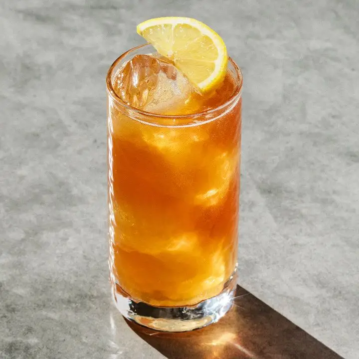 Forbidden Fruit cocktail in a highball glass over ice, with a lemon half-wheel garnish balanced on top