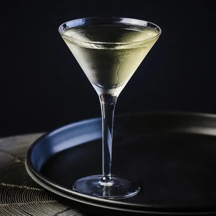 A chilled, yellow-hued Martini served in a clear Martini glass on a round black tray