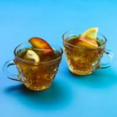 tea for two cocktail served in two ornate punch glasses, each garnished with a lemon half-wheel and peach slice