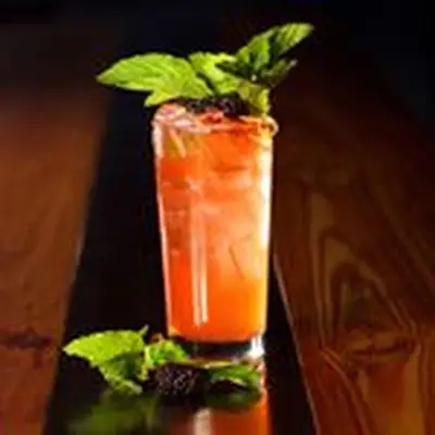 Black-Eyed Rye cocktail in a Highball glass, garnished with mint leaves and three skewered blackberries