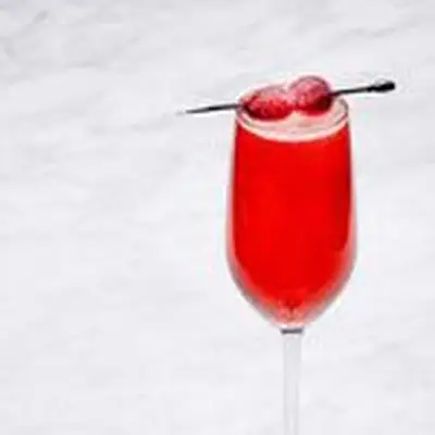 Red Cranberry Ginger Mimosa in flute glass with speared sugared cranberries on marble surface