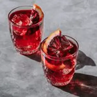 Two rocks glasses on a gray marble surface hold dark red drinks over ice, garnished with blood orange slices.