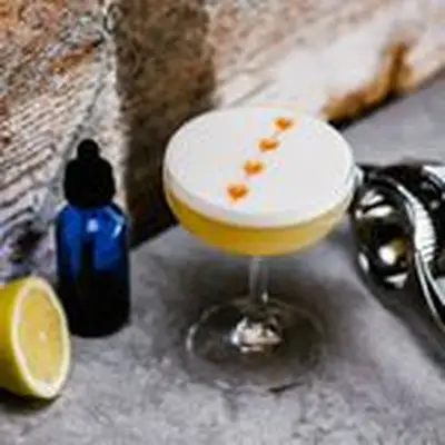 A Whiskey Sour in a coupe glass with a row of bitter drops down the center