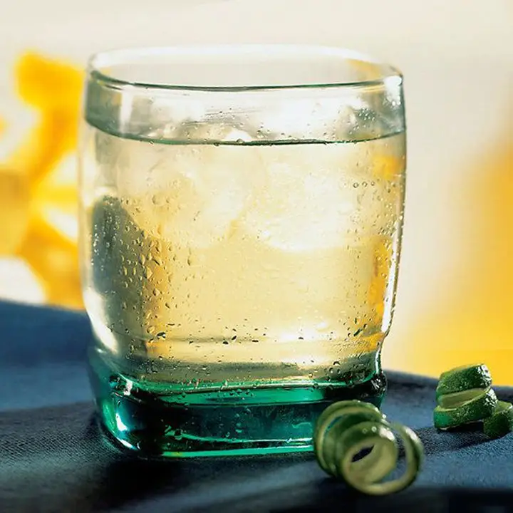 clear chilcano cocktail in a square-shaped rocks glass with ice, sitting beside two curled lime peels