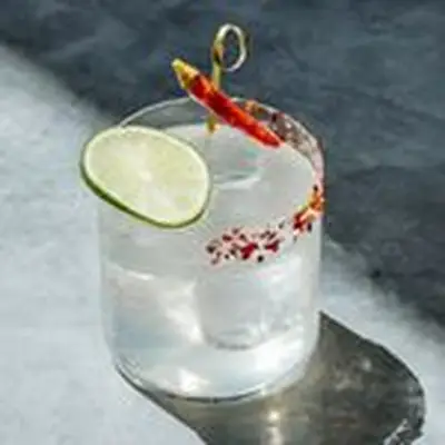 Tom Yum on a Rock cocktail in a rocks glass, garnished with a skewered red chile pepper and a lime wheel