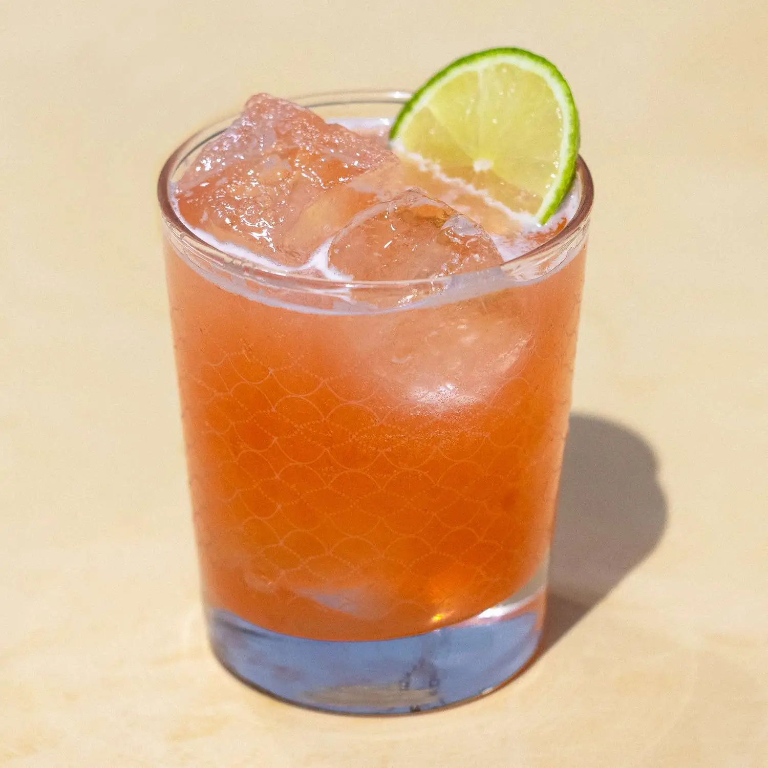 Savory Margarita cocktail served in rocks glass with cubed ice and lime wheel, shot against tan background