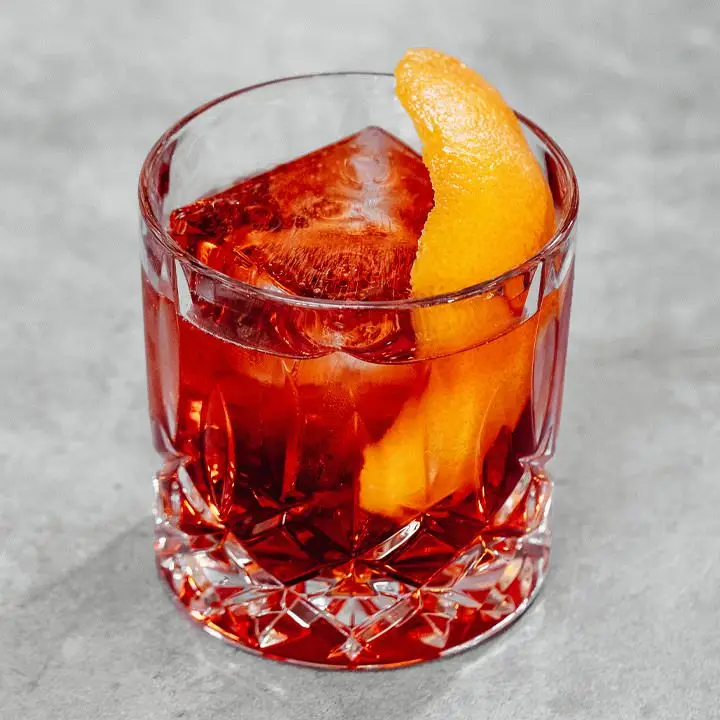 Kingston Negroni cocktail in rocks glass with large ice cube and orange peel, shot on gray marble