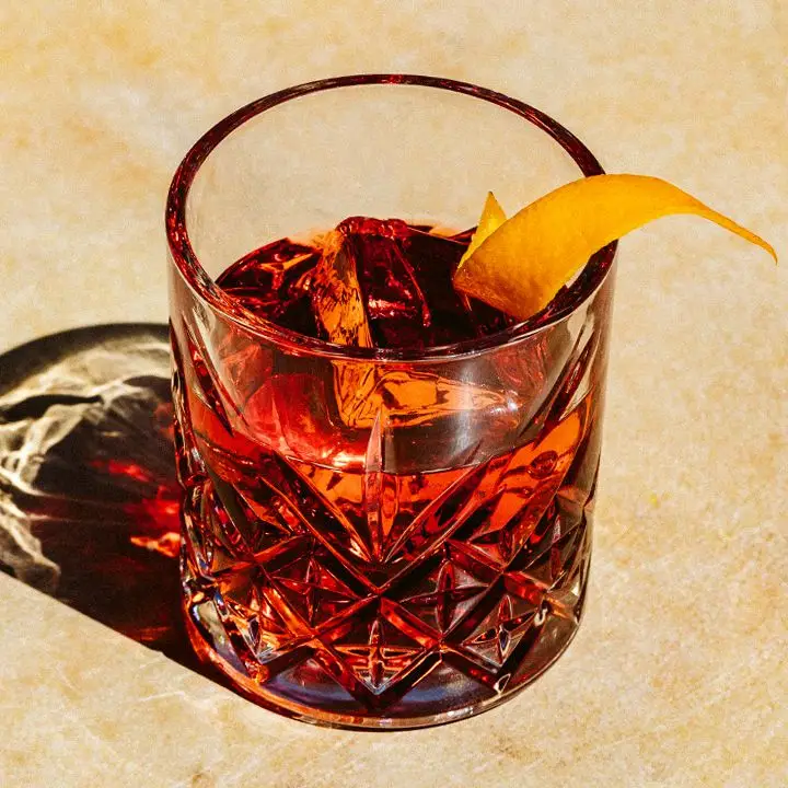 Quill cocktail served in etched rocks glass with large ice cube and orange peel, shot on tan background