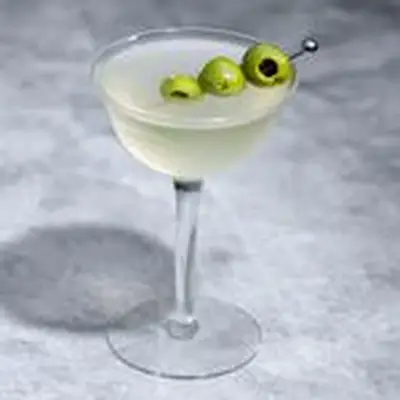 Dirty Martini in a coupe glass with three olives as a garnish, and a side dish of olives in the background