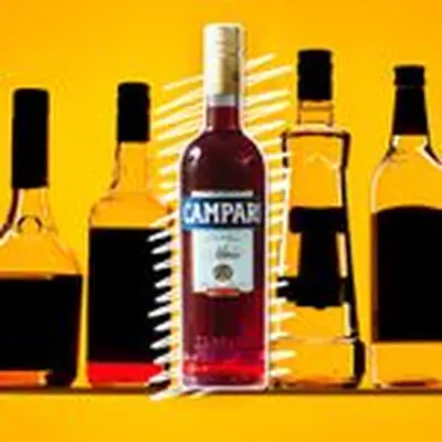 A bottle of ruby-hued Campari sits on a golden background. It is surrounded by other bottles, though their labels are darkened so as to be unreadable