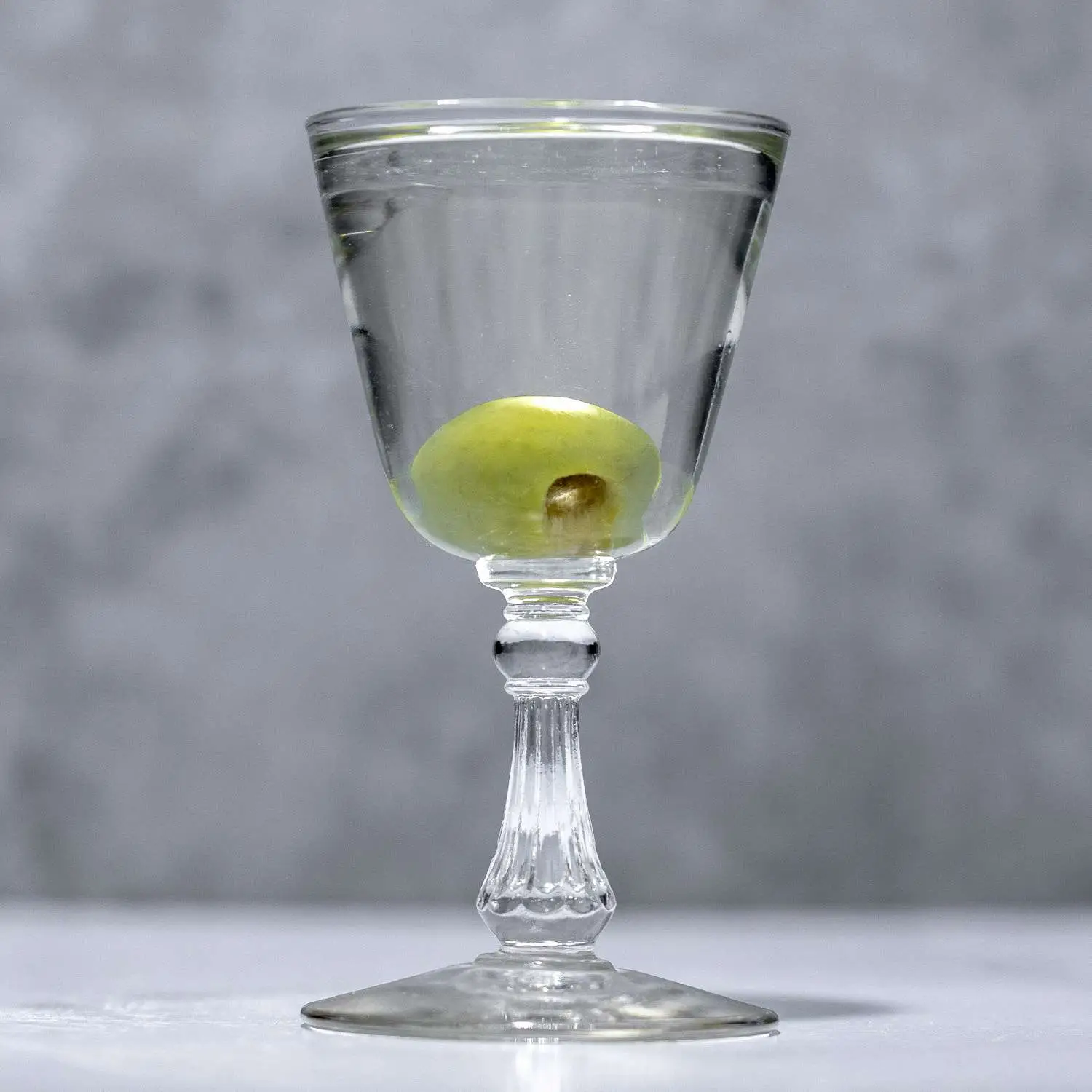 Reverse Martini in a Nick & Nora, sherry-style glass, with dropped olive garnish on marble background