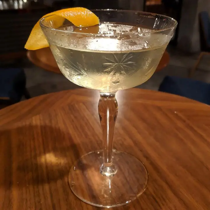 A pale yellow cocktail in a vintage etched cocktail glass garnished with orange zest